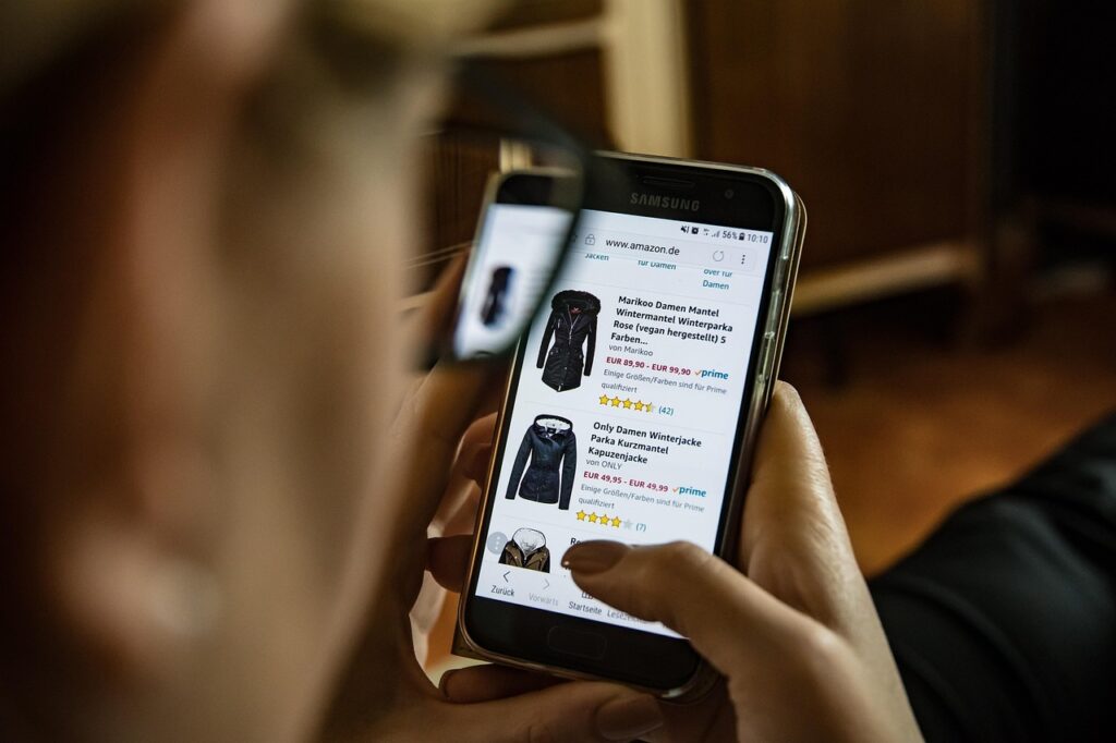 A person shops online using a smartphone, browsing winter jackets on a retail app.